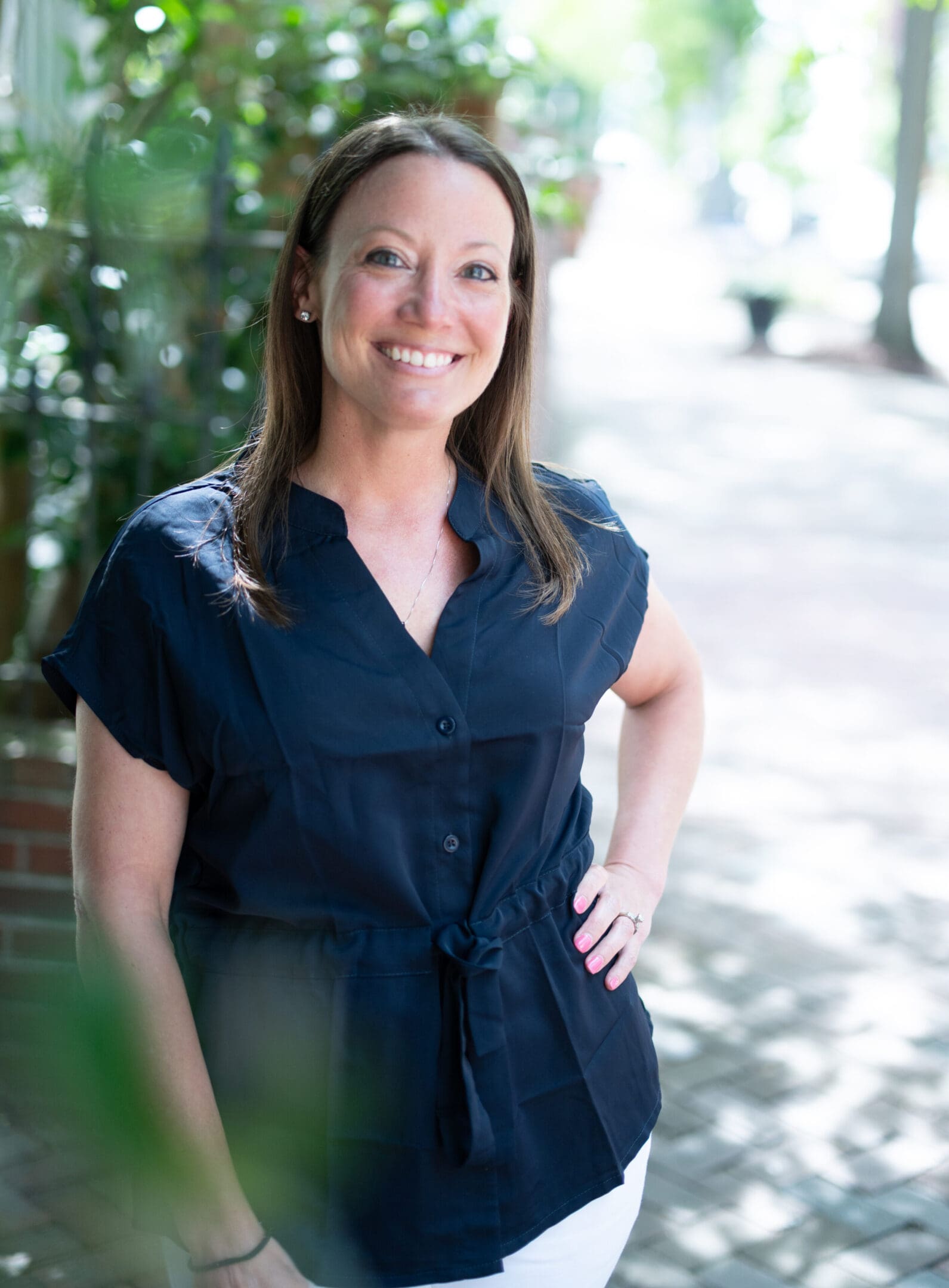 Smiling woman in a navy dress poses outdoors with hand on hip.