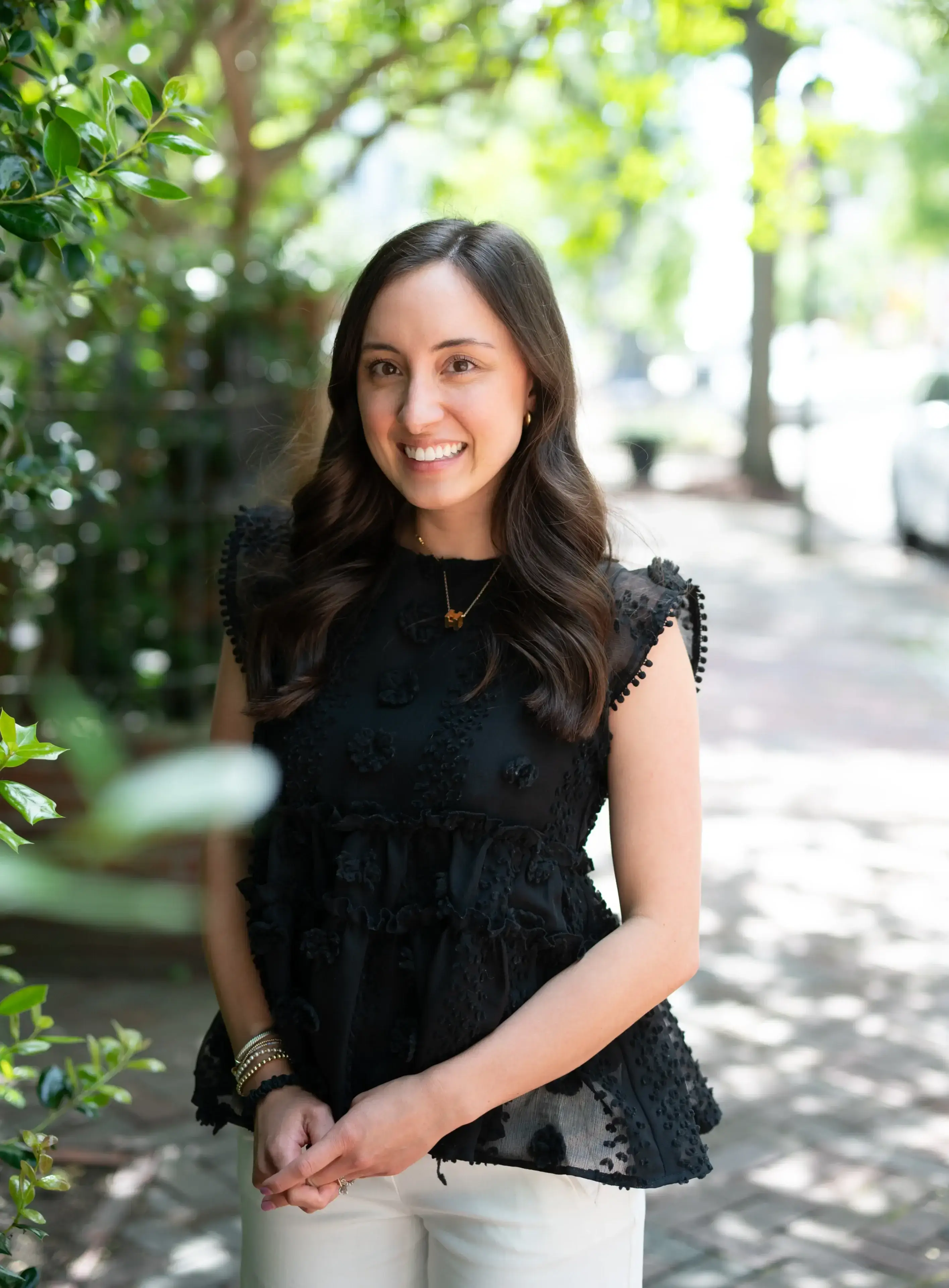 Smiling woman in a black dress outdoors on a sunny day.