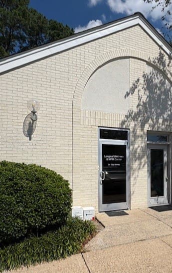 A white brick building with a glass door and a small bush.