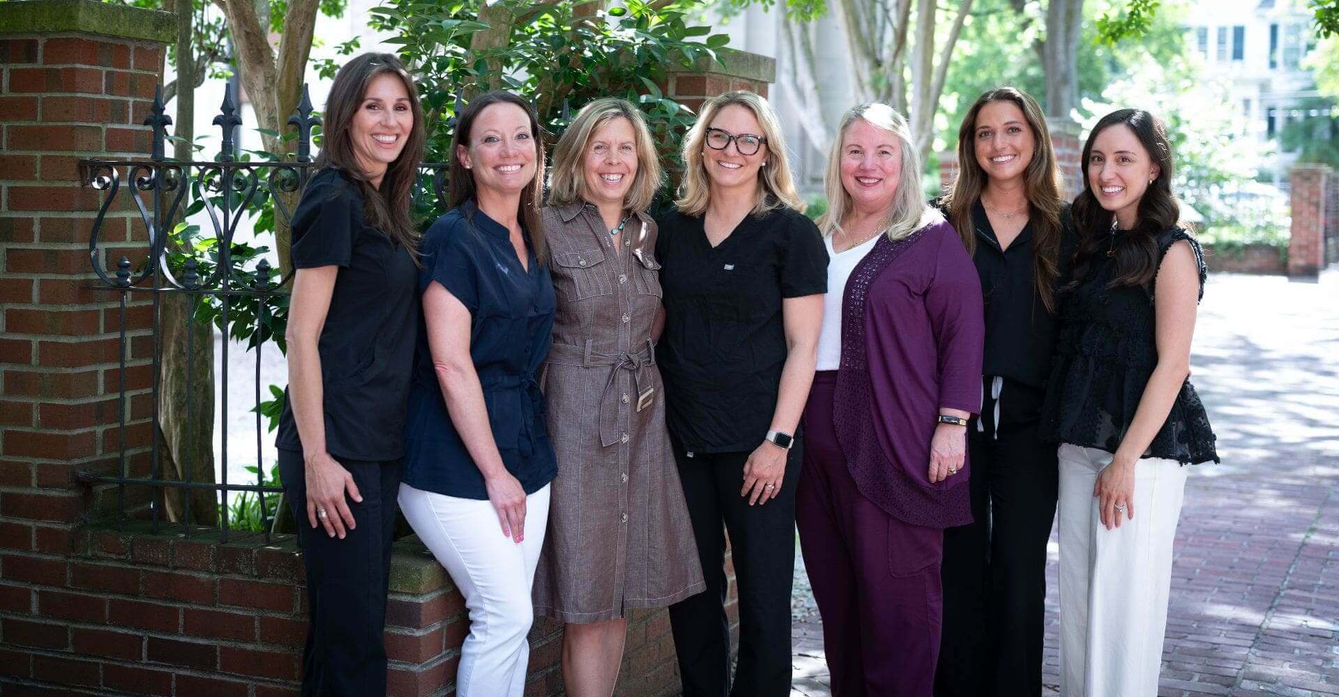 A group of six women standing outdoors, smiling at the camera.